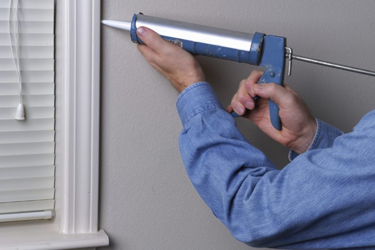 Handyman doing home maintenance. Caulking window trim.